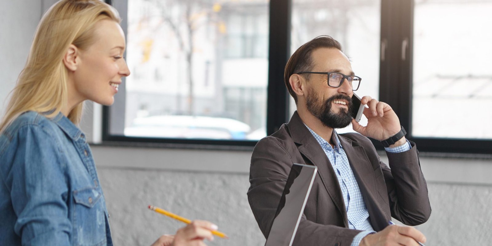 Businesspeople involved in working process. Attractive well skilled bearded elegant man dressed formally, makes busines call, pretty blonde female keyboards report on laptop computer, has good mood